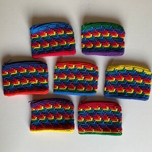 May include: Set of seven rainbow crocheted coin purses. Each purse features a different colour combination of red, orange, yellow, green, blue, indigo, and violet.