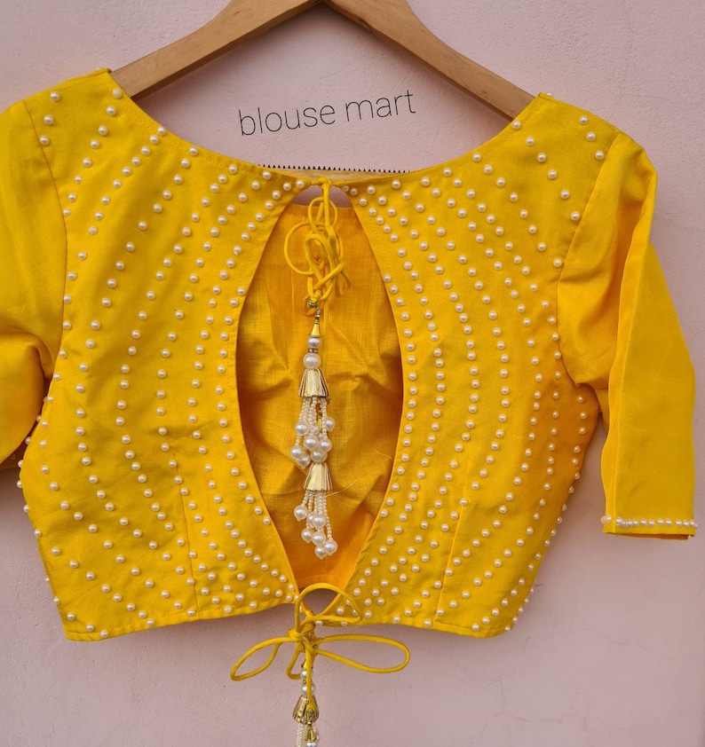 May include: A yellow blouse with a low back and pearl embellishments. The blouse has a tie at the back and a tassel.