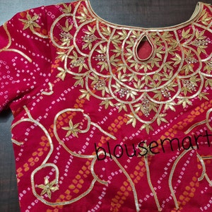 May include: A red blouse with a gold and white embroidered design. The embroidery features a floral pattern with leaves and beads. The blouse has a round neckline and a keyhole opening at the back.