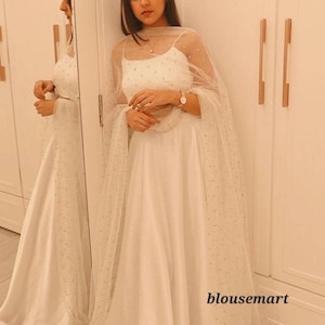 May include: A white maxi dress with a sheer overlay and a white crop top. The dress has a gathered skirt and the top has a scoop neck.