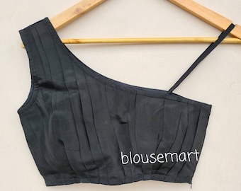 May include: Black one-shoulder blouse with pleats and a single strap. The blouse is cropped and has a zipper closure. The text "blousemart" is visible on the front of the blouse.