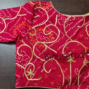 May include: A red and white patterned blouse with gold embroidery and a scoop neckline. The blouse has a "blousemart" watermark.