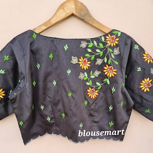 Op de afbeelding: Een zwarte zijden blouse met een gegolfde zoom en een geborduurd bloemenontwerp in tinten groen, geel, oranje en grijs. De blouse heeft een boot hals en korte mouwen. De tekst "blousemart" is zichtbaar onderaan de afbeelding.