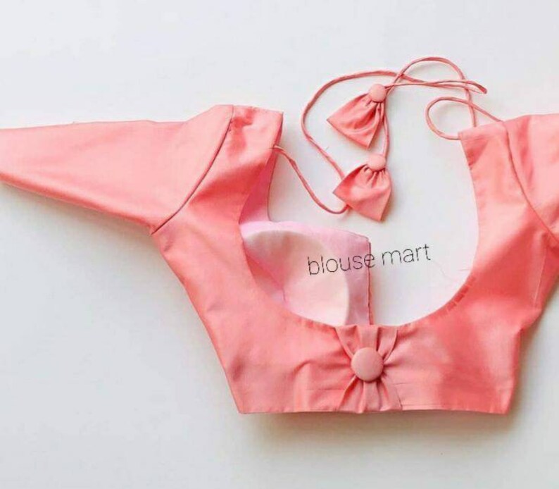 May include: A pink sleeveless blouse with a gathered back detail and a button closure. The blouse has a scoop neck and a tie-up back.