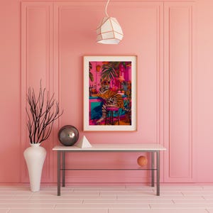 May include: A framed art print shows a tiger in sunglasses at a bar with tropical plants. The artwork is on a white table against a pink wall, with a vase and geometric shapes. The room has a modern design.