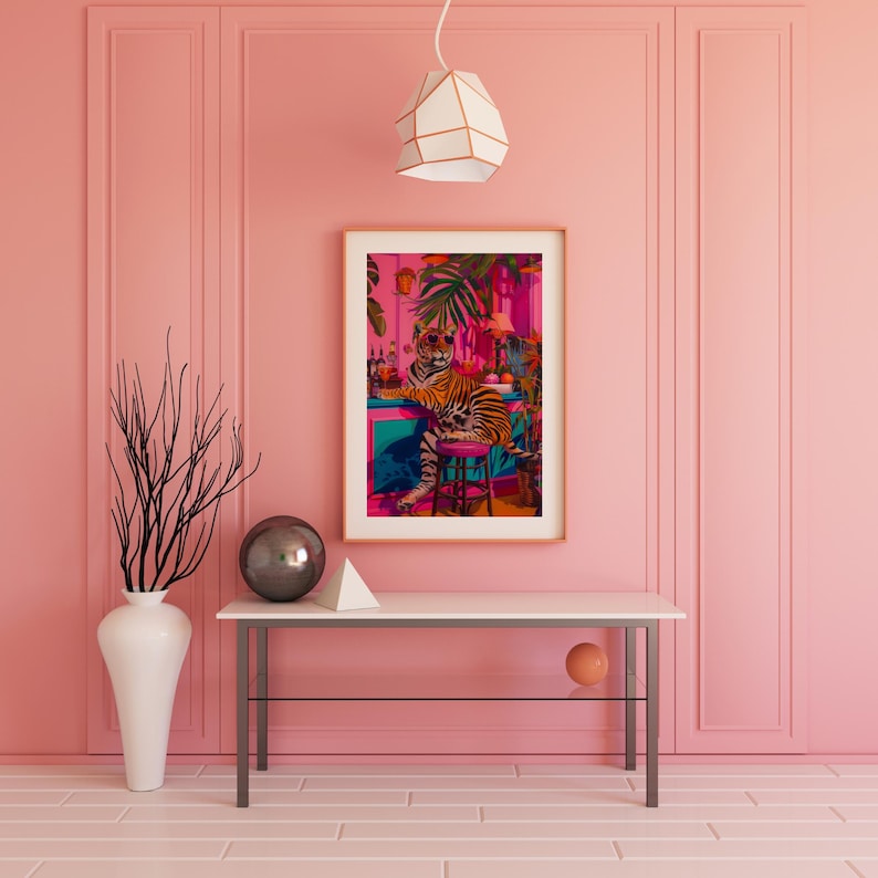 May include: A framed art print shows a tiger in sunglasses at a bar with tropical plants. The artwork is on a white table against a pink wall, with a vase and geometric shapes. The room has a modern design.