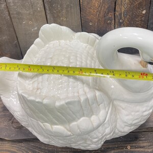 May include: White ceramic swan-shaped serving dish with a textured surface and a raised design. The dish is approximately 11 inches long.