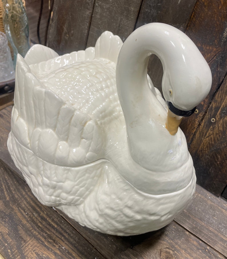 May include: A white ceramic swan shaped serving dish with a lid. The swan's head is turned to the side and the lid is closed.