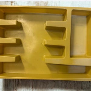 May include: Mustard yellow plastic organizer with multiple compartments. The rectangular tray has various sized sections for storage. The organizer is designed to hold small items and keep them separated. The tray is made of a durable plastic material.
