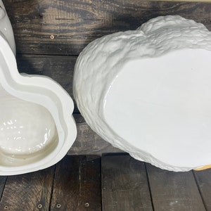 May include: A white ceramic goose cookie jar with a yellow beak and feet. The jar is open and the inside is visible. The jar is sitting on a wooden surface.
