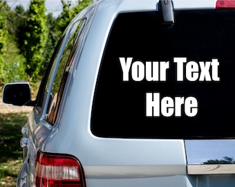 Op de afbeelding: Achterruit van een zilveren SUV met de tekst "Your Text Here" in het wit. Het voertuig heeft een zwarte ruit en een rood achterlicht. De achtergrond toont groene bomen en bladeren.