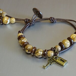 May include: A brown leather bracelet with a key and lock charm. The bracelet is adorned with brown and beige patterned beads.