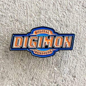 Może przedstawiać: Emaliowana przypinka w kolorze niebieskim i pomarańczowym z napisem "DIGITAL MONSTERS" i "DIGIMON" w pikselowanej czcionce.