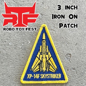 Op de afbeelding: Een gele en blauwe strijk-op patch met een straaljager met de tekst "XP-14F SKYSTRIKER". De patch is driehoekig en meet 7,6 cm.