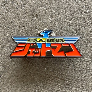 May include: A red, black, and gold enamel pin featuring the Japanese text "超人戦隊バルス" (Chōjin Sentai Balus) with a blue and white eagle wing design.