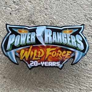Può includere: Un logo Power Rangers Wild Force blu e verde con il testo "20 Years" in giallo. Il logo è su uno sfondo bianco.