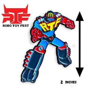 Puede incluir: Un pin de esmalte de robot rojo, azul y amarillo con el texto "RTF" en el pecho. El pin mide 5 cm de alto.
