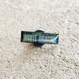 May include: A black and silver pin with the text "Legend of the White Dragon" on it.
