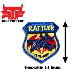 Peut inclure: Patch brodé représentant un bouclier bleu et jaune avec le texte "RATTLER" et "VTOL-86B". Le bouclier présente un avion à réaction rouge et bleu avec des flammes sur un fond jaune. Le patch mesure 2,5 pouces.