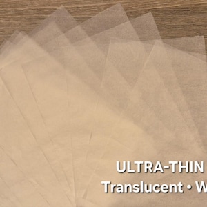 Può includere: Una disposizione a ventaglio di fogli rettangolari di carta traslucida color bianco sporco. Il testo "ULTRA-THIN ART PAPER" e "Translucent • Wet Strength" è stampato in bianco nell'angolo in basso a destra dell'immagine.