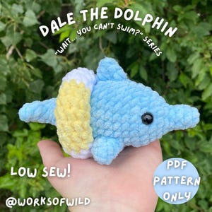 Op de afbeelding: Een lichtblauw gehaakt dolfijn speelgoed met witte en gele accenten. De dolfijn heeft een zwart oog en maakt deel uit van de "Wait... You Can't Swim?" serie. Tekst op de afbeelding luidt "Dale the Dolphin", "Low Sew!" en "PDF Pattern Only".