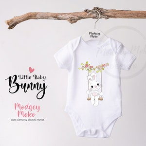 May include: White baby onesie with a cute cartoon bunny on a swing with pink flowers. The onesie has the text "Little Baby Bunny" and "Modgey Moko" on it.