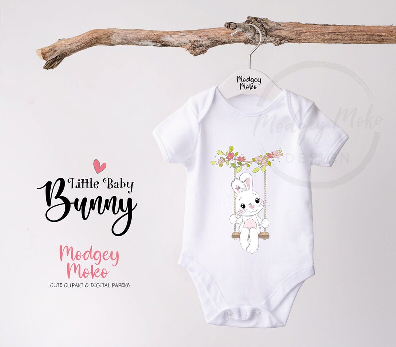 May include: White baby onesie with a cute cartoon bunny on a swing with pink flowers. The onesie has the text "Little Baby Bunny" and "Modgey Moko" on it.