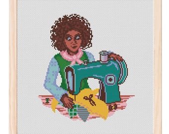 May include: Cross-stitch artwork of a person sewing with a teal sewing machine. The person is wearing a green vest, a pink scarf, and a light blue shirt. The artwork is framed in a light wood frame.