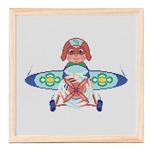 May include: Cross-stitch artwork of a cartoon pilot in a biplane. The pilot has brown hair, goggles, and a green outfit. The biplane is blue with green and yellow floral accents. The artwork is framed in a light wood frame.