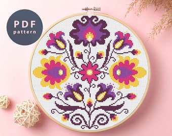 May include: A cross-stitch pattern featuring a floral design with yellow, pink, purple, and black flowers on a white background. The pattern is in a round wooden embroidery hoop.