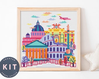 May include: A counted cross stitch kit featuring a colorful cityscape with buildings, a plane, and clouds. The kit includes all the materials needed to complete the project.
