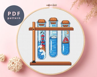 May include: Cross stitch pattern of three glass test tubes with cork tops, each containing a different nautical scene: a lighthouse, a sailboat, and a moon and stars. The test tubes are on a wooden stand.