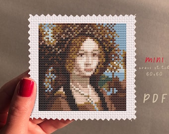 May include: A cross stitch pattern of a woman with brown hair and a blue background. The pattern is 60 stitches by 60 stitches and is labeled "mini cross stitch 60x60 PDF".