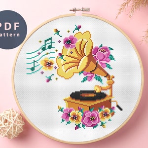 May include: Cross stitch pattern of a vintage record player with flowers and musical notes. The record player is yellow and gold with a black record. The flowers are pink, yellow, and green.