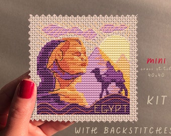 May include: A cross stitch kit featuring a purple and orange illustration of the Great Sphinx of Giza and a camel in the desert. The kit includes back stitches and is 40x40 stitches.