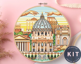 May include: Counted cross stitch kit featuring a colorful pixelated image of the Roman Colosseum and other buildings. The kit includes all the materials needed to complete the project.  The text "COUNTED KIT CROSS STITCH" is printed on a blue circle.