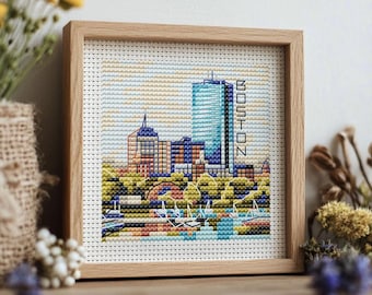 May include: Cross-stitch artwork of the Boston skyline, framed in light wood. The design features a detailed depiction of the city's buildings, trees, and water, with the word "BOSTON" vertically stitched on the right side.
