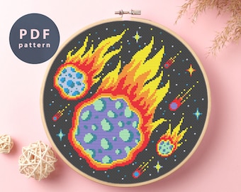 May include: A cross-stitch pattern featuring a fiery comet with a purple and green core, surrounded by smaller comets and stars on a black background.