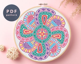 May include: A colorful cross-stitch pattern in a wooden embroidery hoop. The pattern features a circular design with intricate details in shades of pink, green, yellow, blue, and purple.