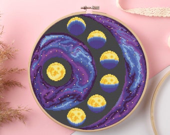 May include: A purple and blue galaxy-themed cross-stitch pattern with a circle of yellow moons in different phases. The pattern is framed in a wooden hoop.