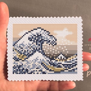 Op de afbeelding: Mini kruissteek van een golf, met tinten blauw, wit en bruin. Het ontwerp staat op witte stof met een geschulpte rand. De tekst "mini cross stitch 50x40 PDF" is zichtbaar.