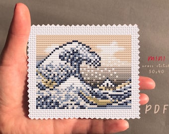 May include: Mini cross stitch of a wave, featuring shades of blue, white, and tan. The design is on white fabric with a scalloped edge. The text "mini cross stitch 50x40 PDF" is visible.