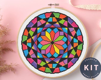 May include: A colorful cross-stitch kit featuring a geometric design in a wooden embroidery hoop. The design includes a vibrant array of colors, including pink, orange, yellow, green, blue, and purple. The kit includes the text "COUNTED KIT CROSS-STITCH".