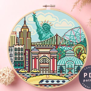 May include: Counted cross stitch pattern PDF of a colourful New York City skyline with the Statue of Liberty, skyscrapers, and a Ferris wheel. The pattern is in a circular hoop.