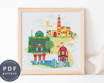 May include: A counted cross stitch pattern featuring a colorful illustration of a cityscape with buildings, palm trees, and a blue sky. The pattern is framed in a light wood frame.
