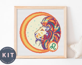 May include: A counted cross stitch kit featuring a colorful, geometric lion with a stylized mane. The lion is surrounded by a yellow and orange sunburst design. The zodiac symbol for Leo is in the lower right corner.