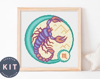 May include: A cross-stitch pattern kit featuring a purple and orange scorpion in a teal circle with a yellow background. The scorpion is surrounded by gold stars and mountains. The letter "m" is in the bottom right corner of the circle.