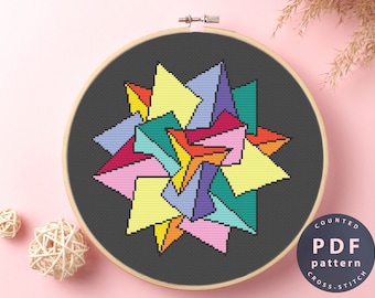 May include: A counted cross stitch pattern featuring a colorful geometric design with a starburst shape. The pattern is printed on a black background and is framed in a wooden hoop. The text "COUNTED PDF pattern CROSS-STITCH" is printed on a white circle in the lower right corner of the image.