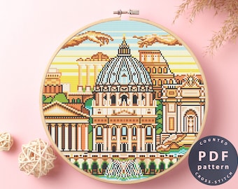 May include: Counted cross stitch pattern PDF for a colorful pixel art design of the Roman Colosseum and surrounding buildings. The design features a blue sky with white clouds and a hand reaching down from the sky.