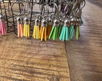 May include: A collection of colorful keychains with tassels. The keychains are made of metal and have a silver finish. The tassels are made of a soft, fuzzy material and come in a variety of colors, including pink, yellow, green, and blue.